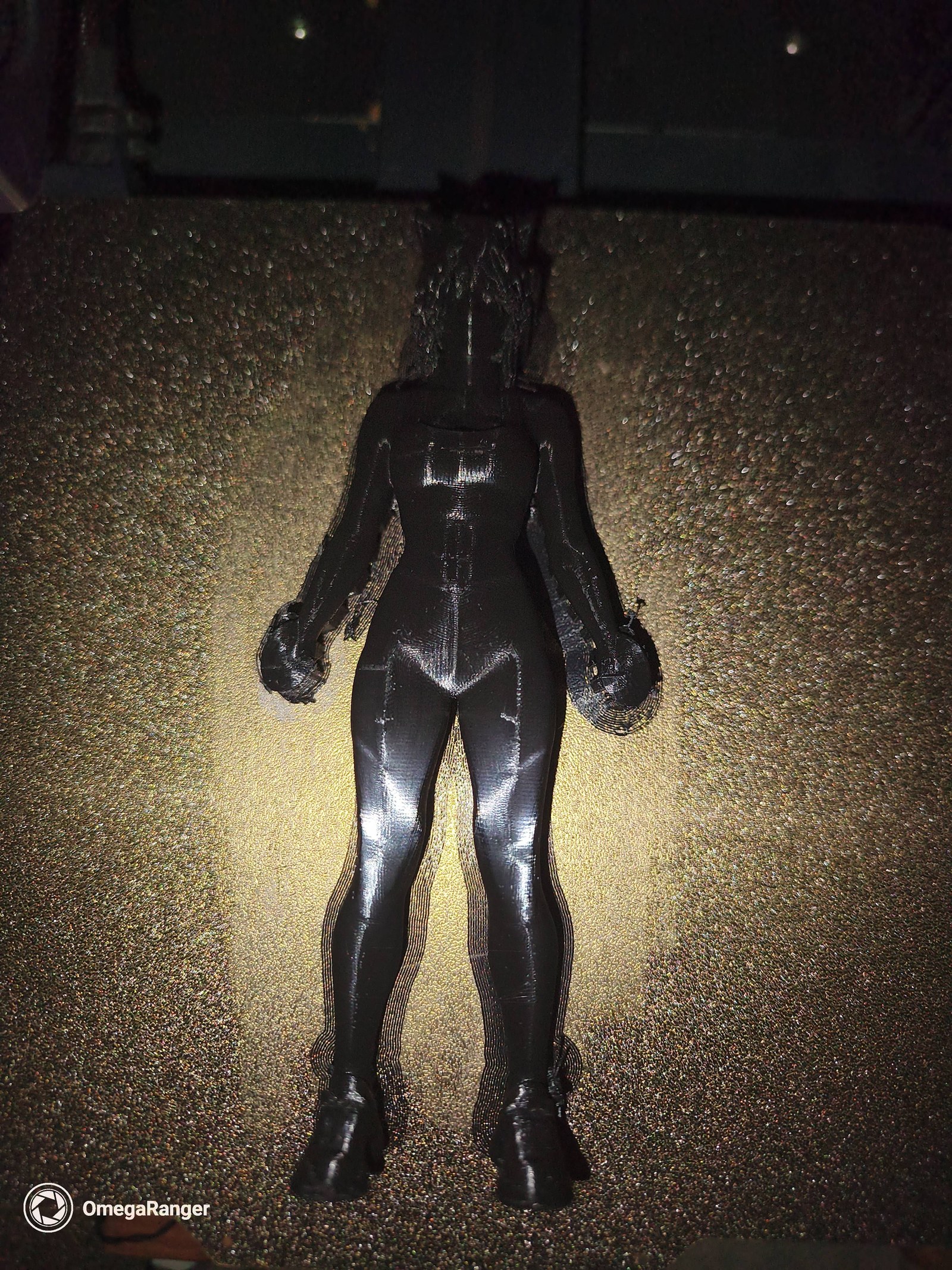 Black FDM print of Neko Omega still on the PEI bed, brim attached, standing without a hand on her